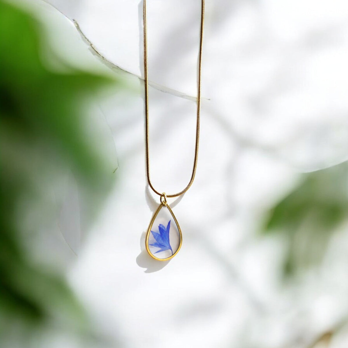 Drupt gouden ketting met druppelvormige hanger waarin een echte blauwe korenbloem is verwerkt.