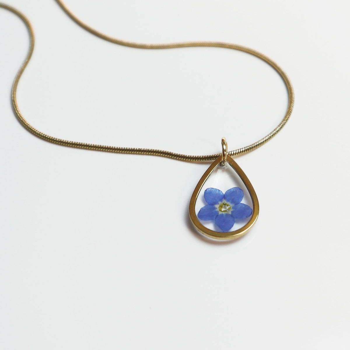 Drupt gouden ketting met een minimalistische druppelvormige hanger en een echt blauw vergeet-me-nietje bloemetje.