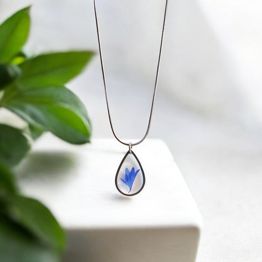 Drupt zilveren druppelvormige hanger met een echte blauwe korenbloem, minimalistisch handgemaakt sieraad aan ketting.