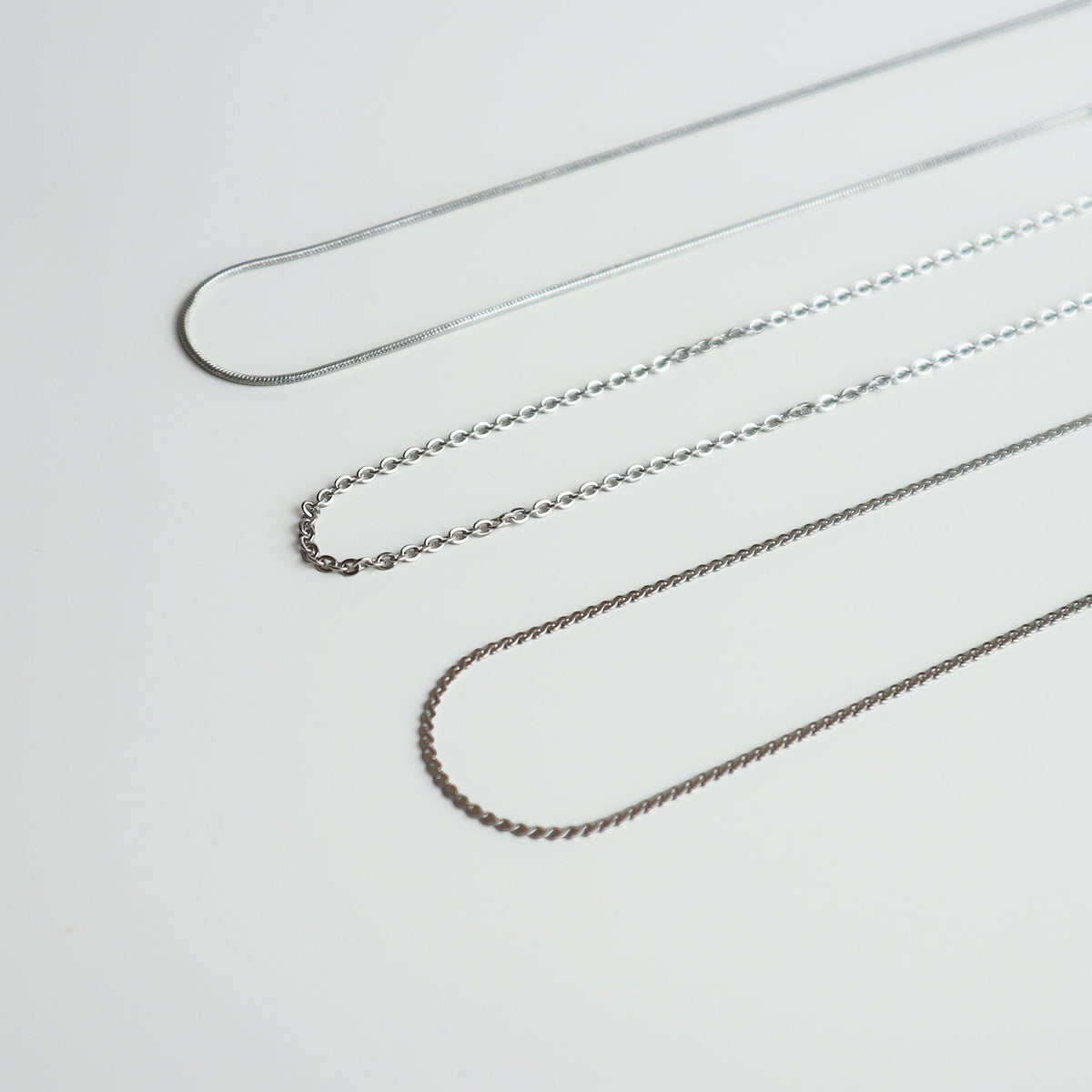 Drie verschillende zilverkleurige kettingen van Drupt op een witte achtergrond voor bij een hanger.