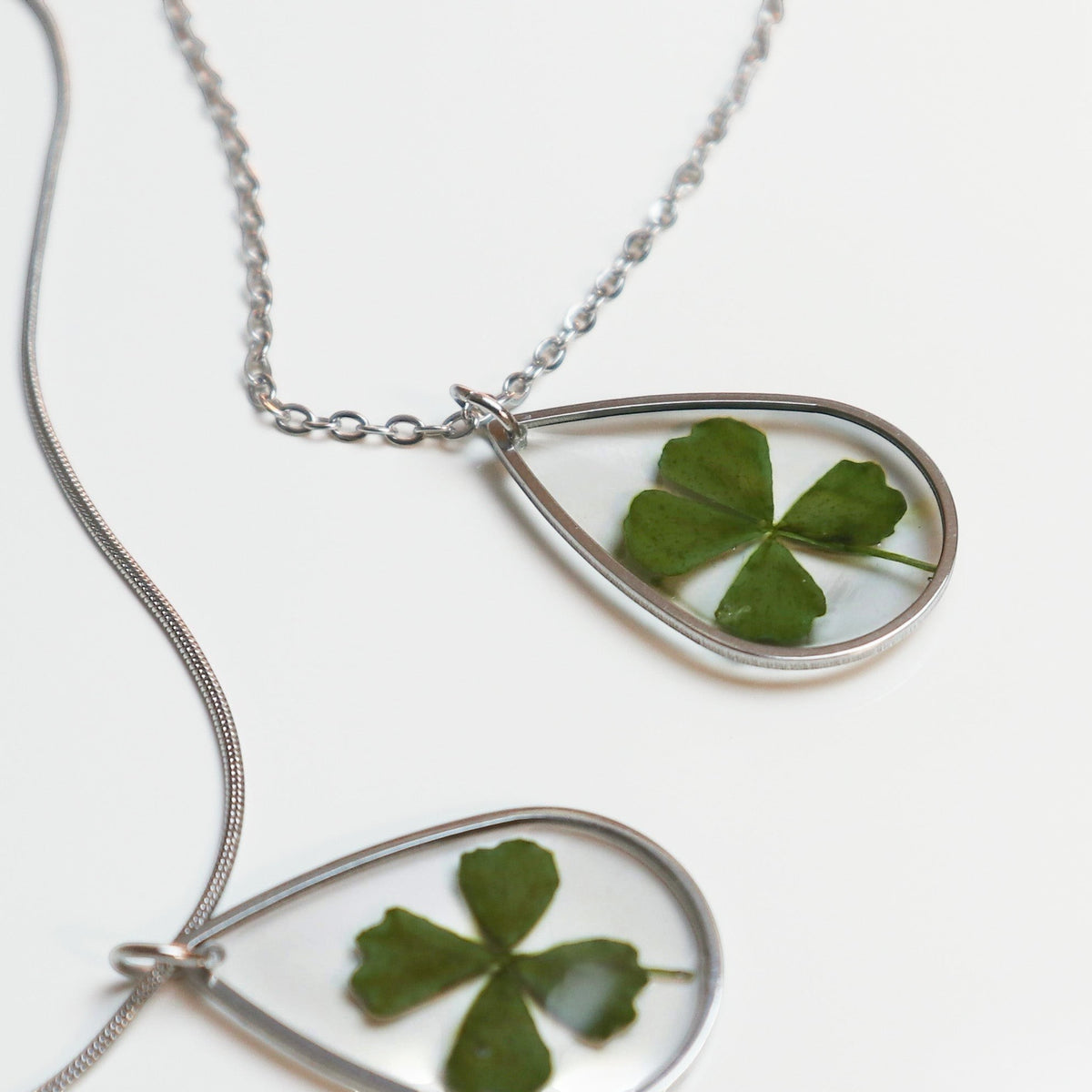 Drupt zilveren druppelvormige ketting met een echt klavertjevier in een minimalistisch handgemaakt sieraad