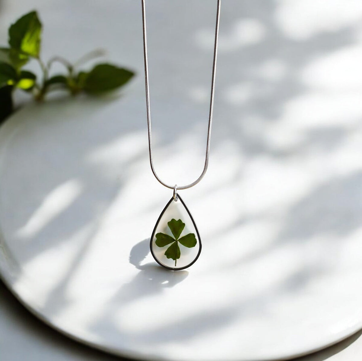 Drupt zilveren druppelvormige ketting met een echt klavertjevier in hars, minimalistisch en handgemaakt sieraad.