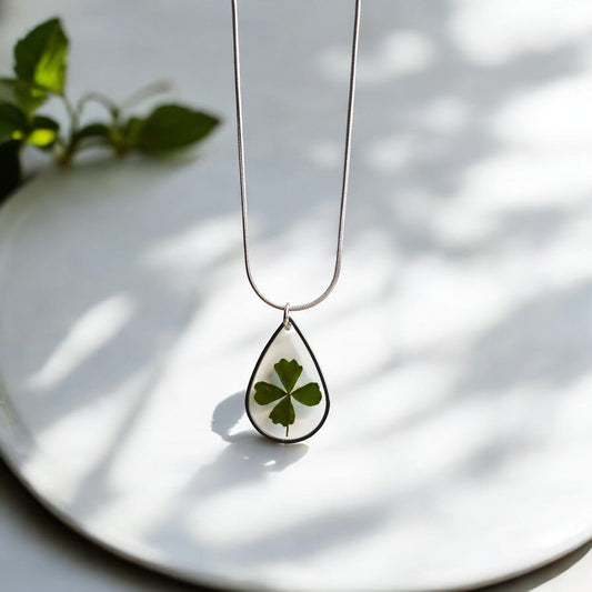 Drupt zilveren druppelvormige ketting met een echt klavertjevier in hars, minimalistisch en handgemaakt sieraad.