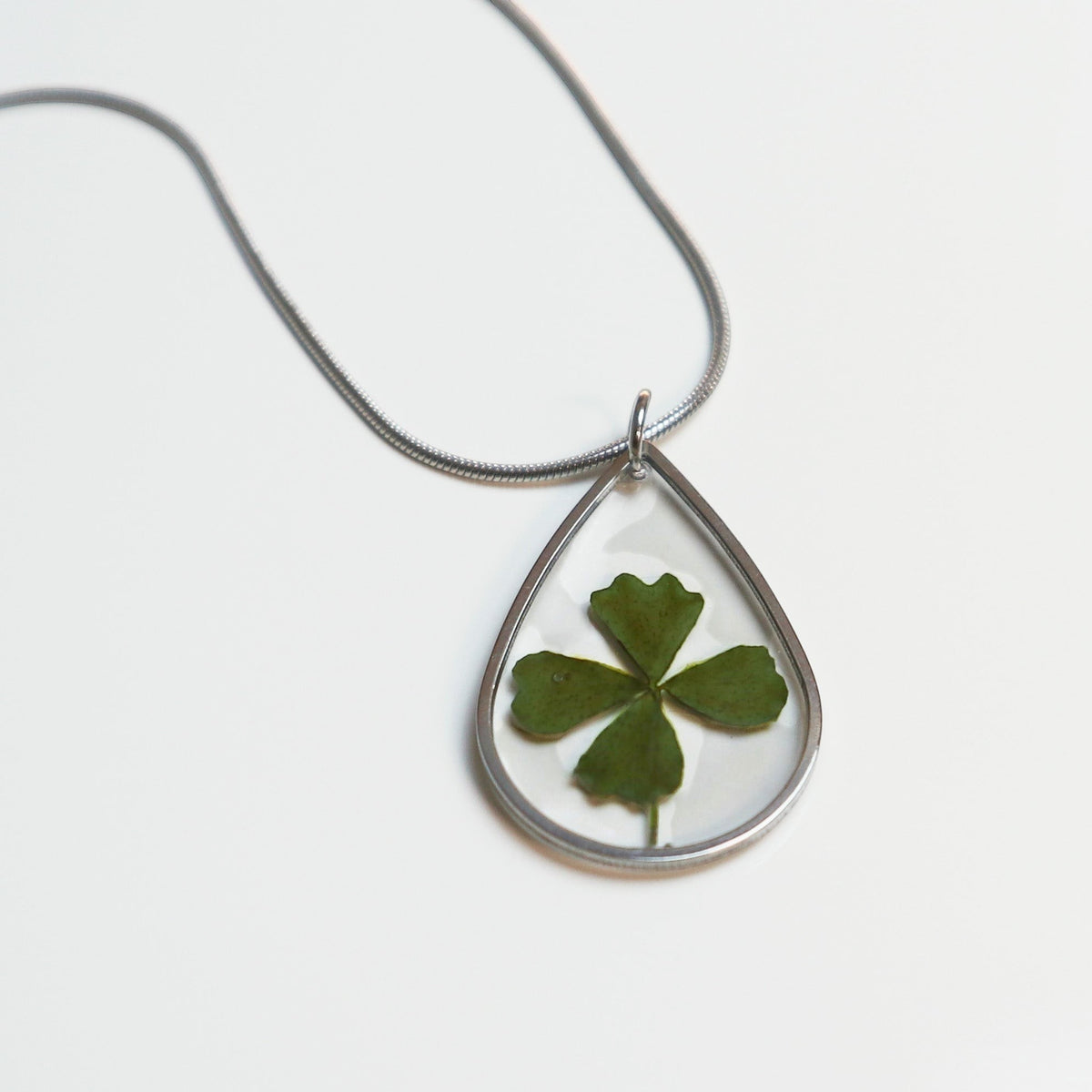 Drupt zilveren druppelvormige ketting met een echt klavertjevier in hars, minimalistisch handgemaakt sieraad.