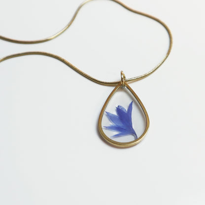 Drupt gouden druppelvormige ketting met een echte blauwe korenbloem in een minimalistisch handgemaakt sieraad.