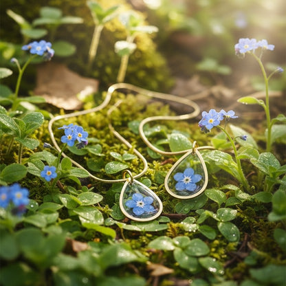 Drupt gouden druppelvormige hanger met echt vergeet-mij-nietje in een bosrijke omgeving met blauwe bloemen