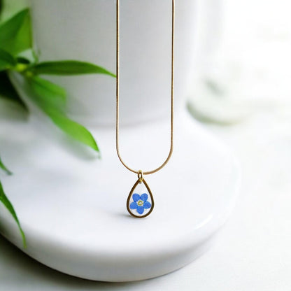 Drupt gouden druppelvormige ketting met een echt gedroogd blauw vergeet-mij-nietje in een minimalistisch design