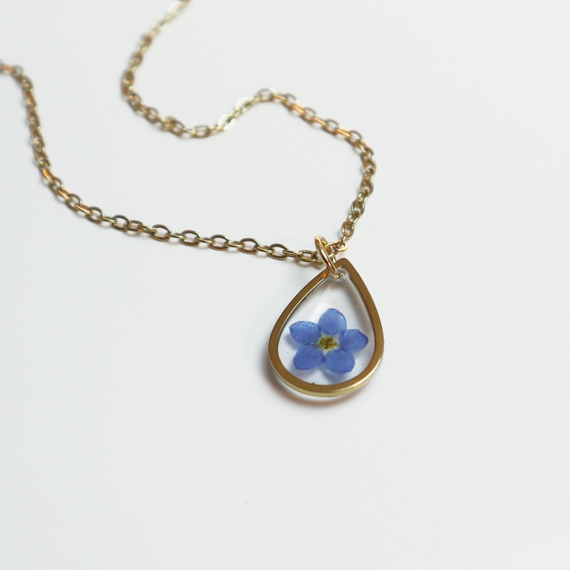 Drupt gouden druppelvormige ketting met een echt gedroogd blauw vergeet-mij-nietje in een minimalistisch design.