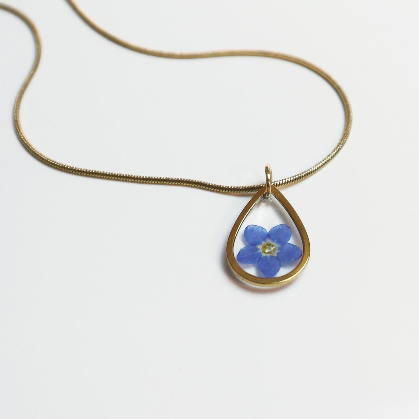 Drupt gouden ketting met een minimalistische druppelvormige hanger en een echt blauw vergeet-me-nietje bloemetje.