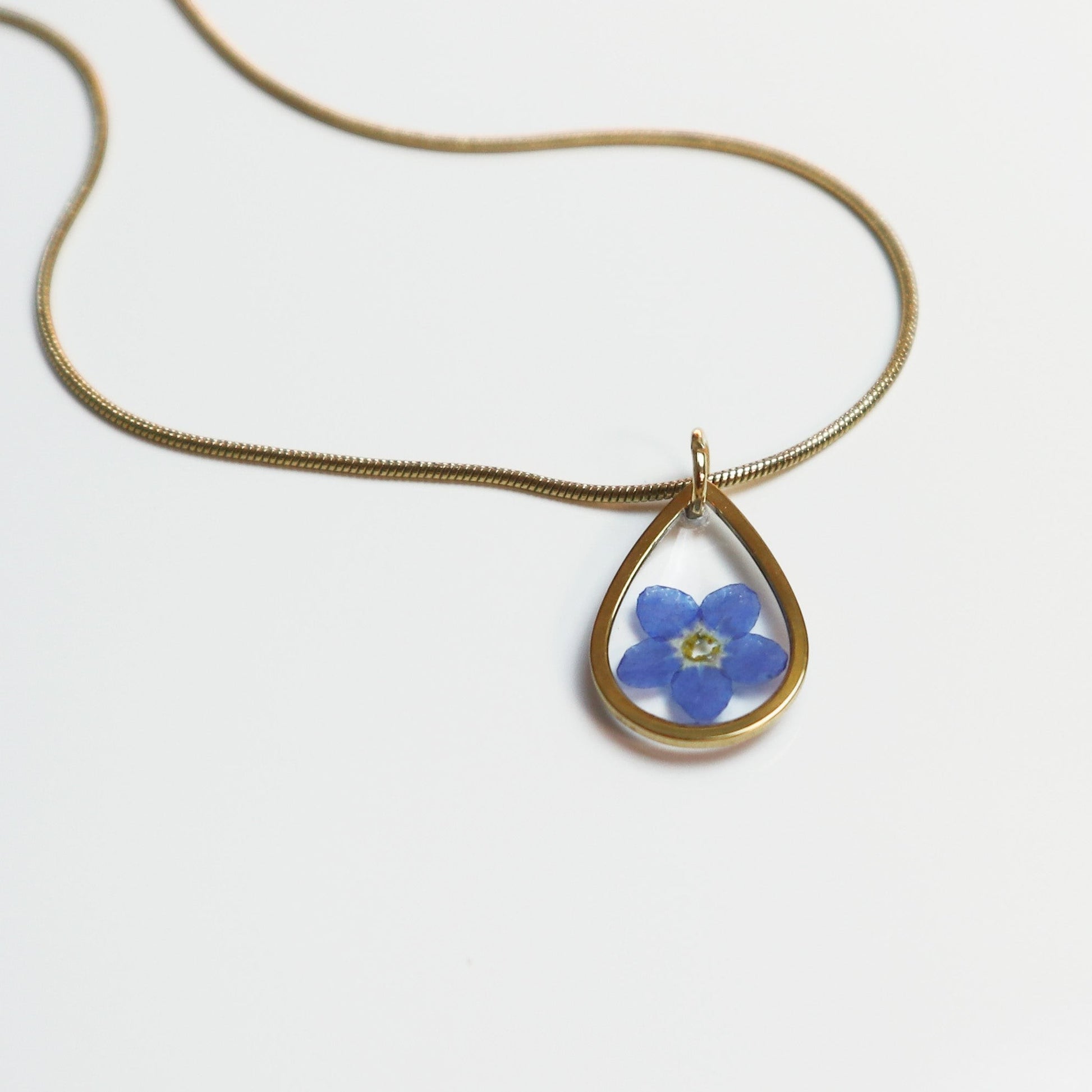 Drupt gouden ketting met een minimalistische druppelvormige hanger en een echt blauw vergeet-me-nietje bloemetje.