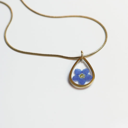 Drupt gouden ketting met een minimalistische druppelvormige hanger en een echt blauw vergeet-me-nietje bloemetje.