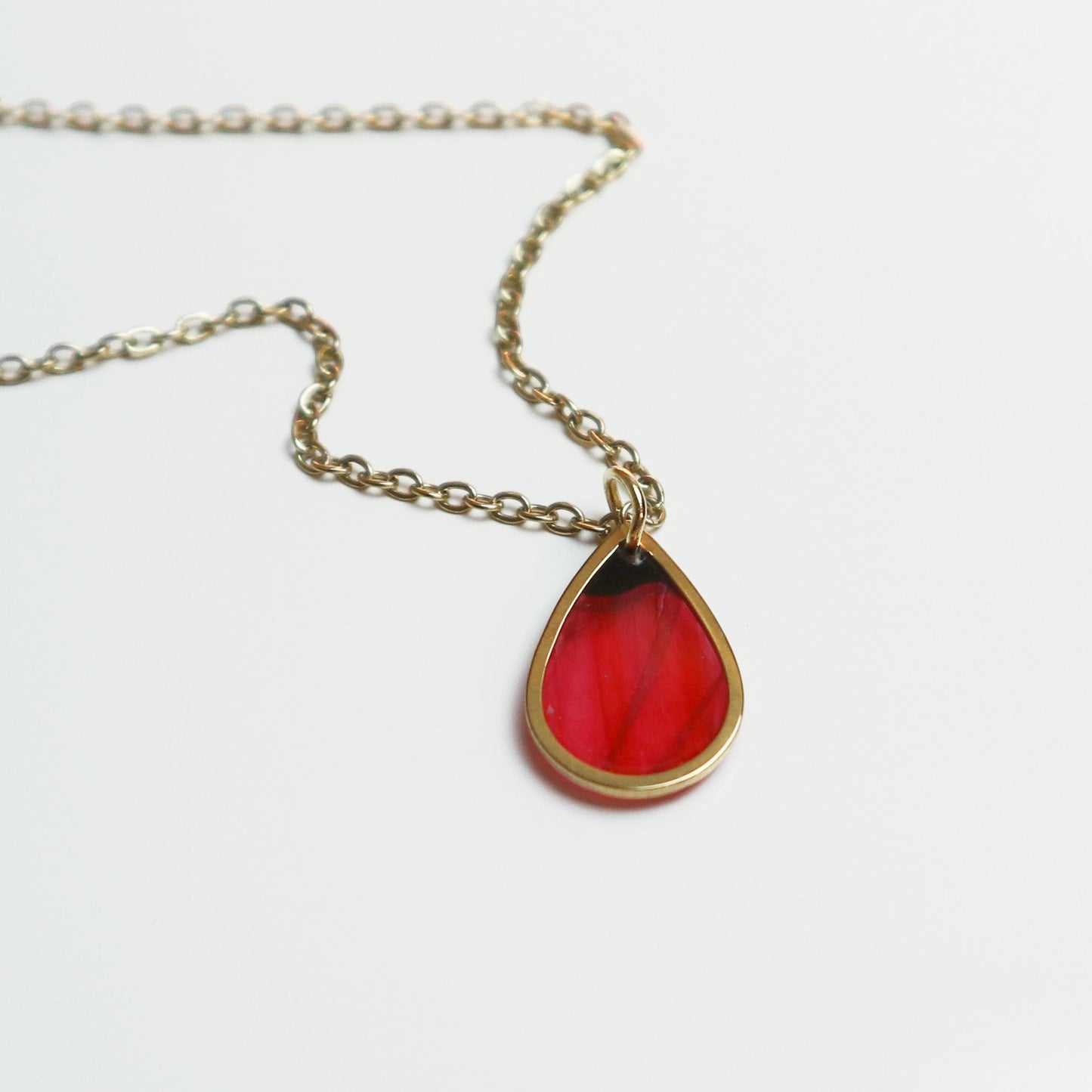 Drupt gouden ketting met druppelvormige hanger waarin een rode klaproos is verwerkt voor een minimalistische look.