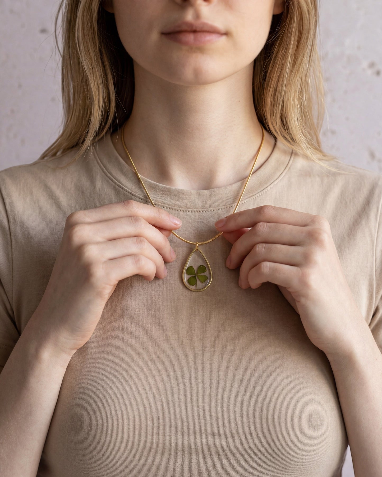 Drupt gouden druppelvormige hanger met echt klavertjevier gedragen aan een subtiele ketting door een vrouw.