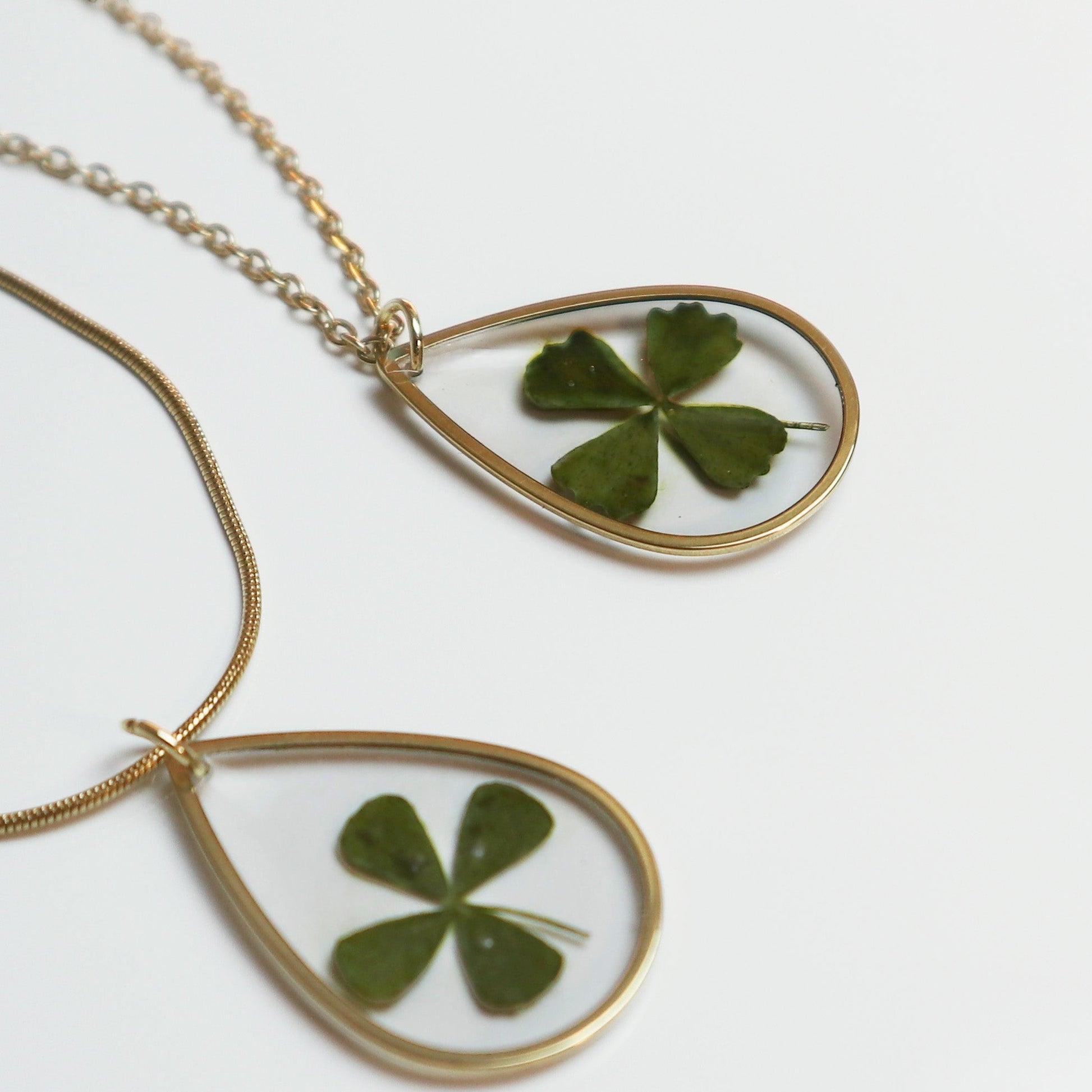 Drupt gouden druppelvormige hanger met een echt klavertjevier, minimalistisch handgemaakt sieraad aan een ketting.