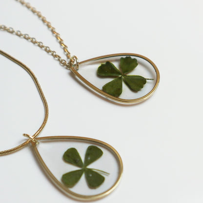 Drupt gouden druppelvormige hanger met een echt klavertjevier, minimalistisch handgemaakt sieraad aan een ketting.
