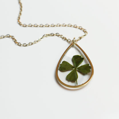 Drupt gouden druppelvormige hanger met een echt klavertjevier, minimalistisch handgemaakt sieraad aan een fijne ketting.