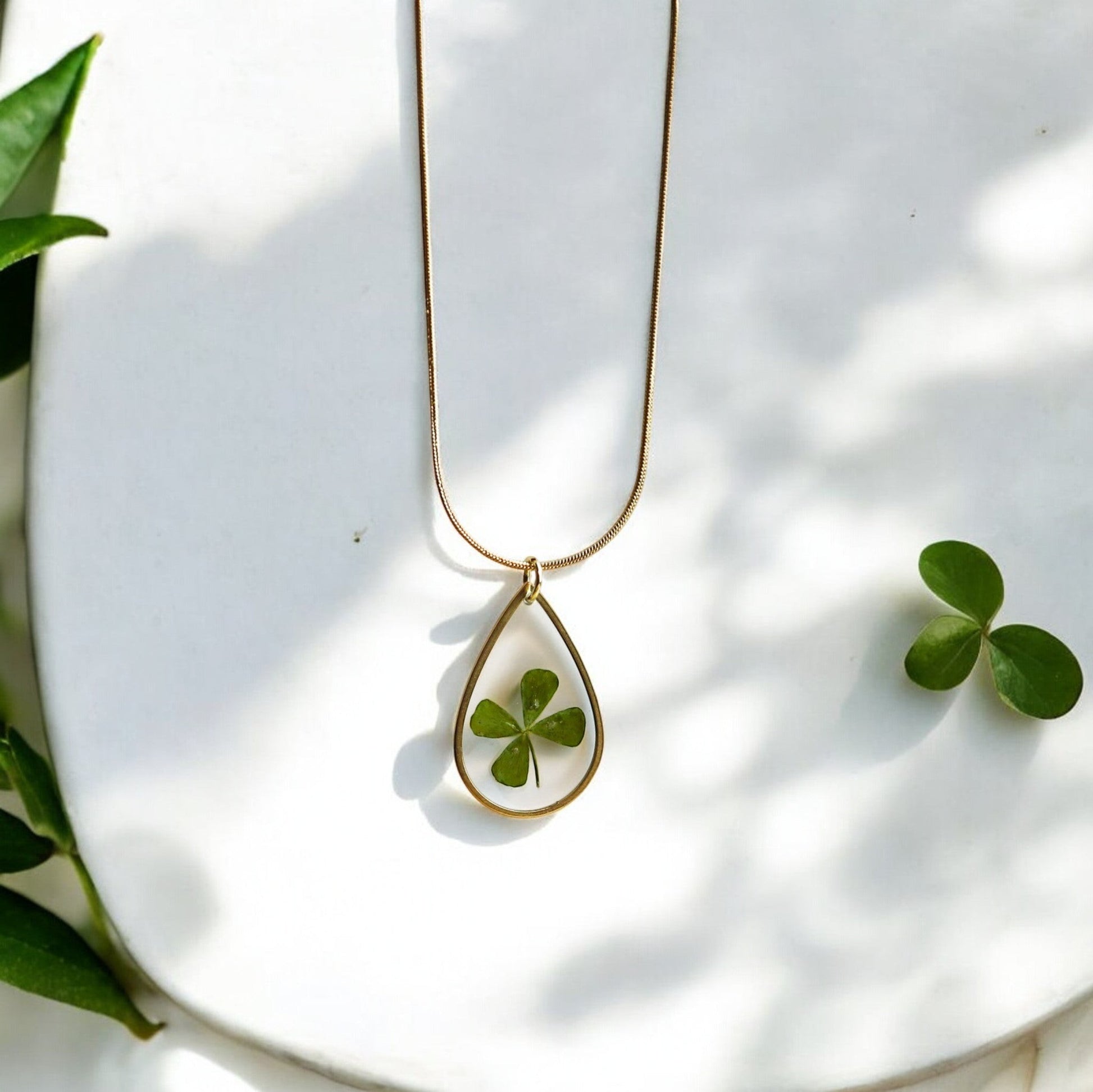 Drupt gouden druppelvormige ketting met een echt klavertjevier in een minimalistisch handgemaakt sieraad