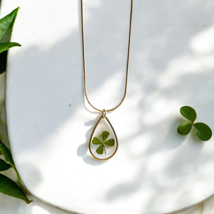 Drupt gouden druppelvormige ketting met een echt klavertjevier in een minimalistisch handgemaakt sieraad