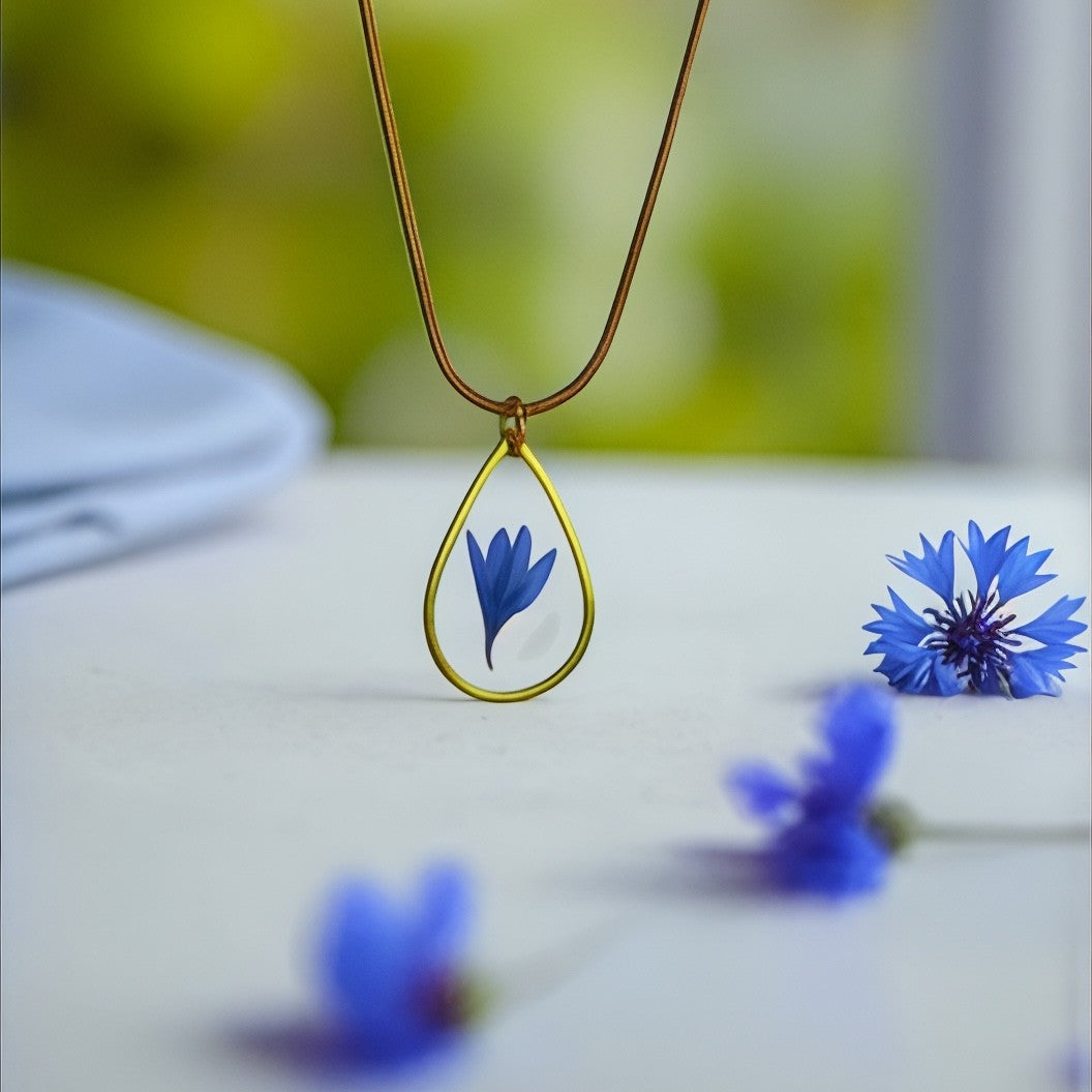 Drupt gouden druppelvormige hanger met een echte blauwe korenbloem, minimalistisch handgemaakt sieraad.