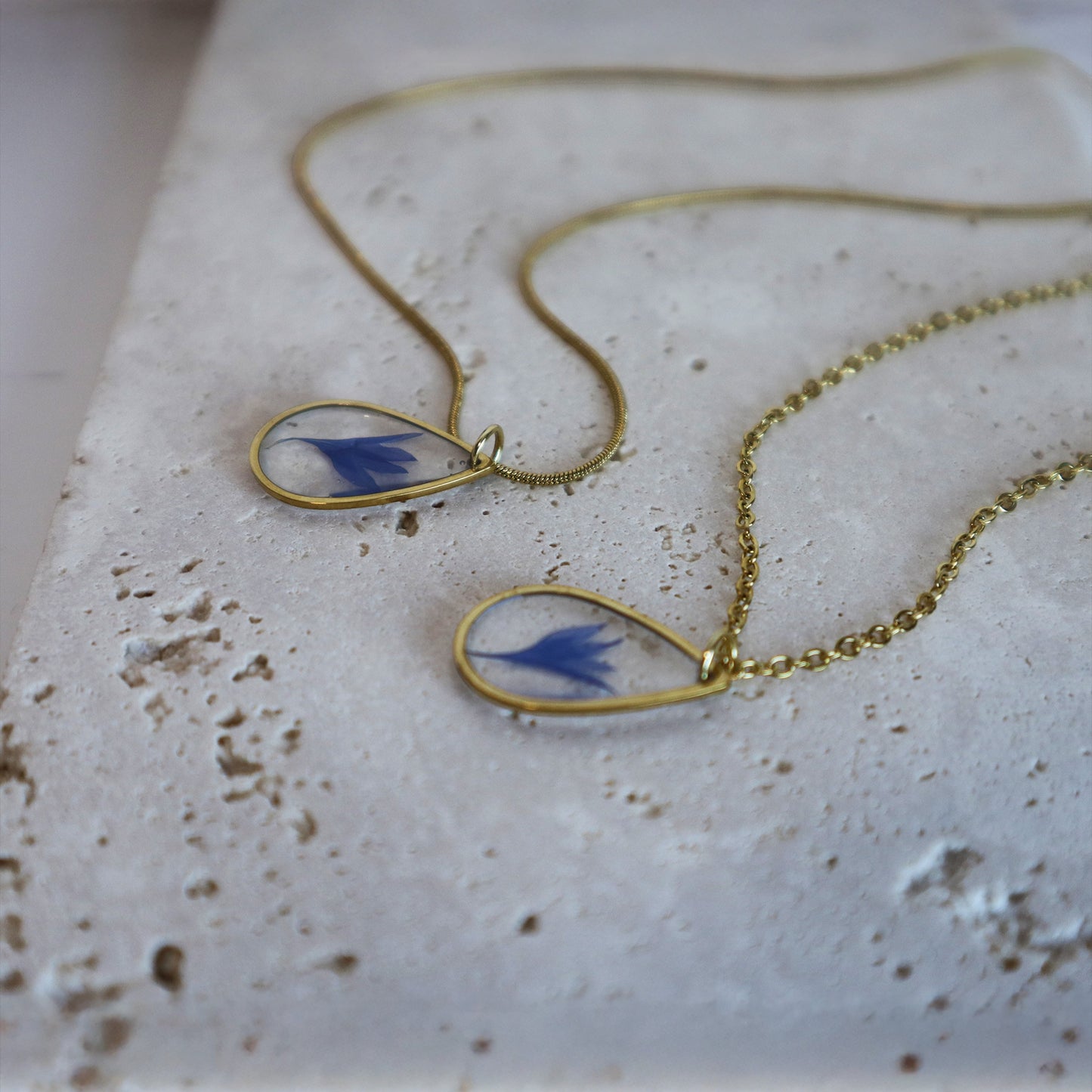 Drupt gouden ketting met druppelvormige hanger en echte blauwe korenbloem op een stenen ondergrond