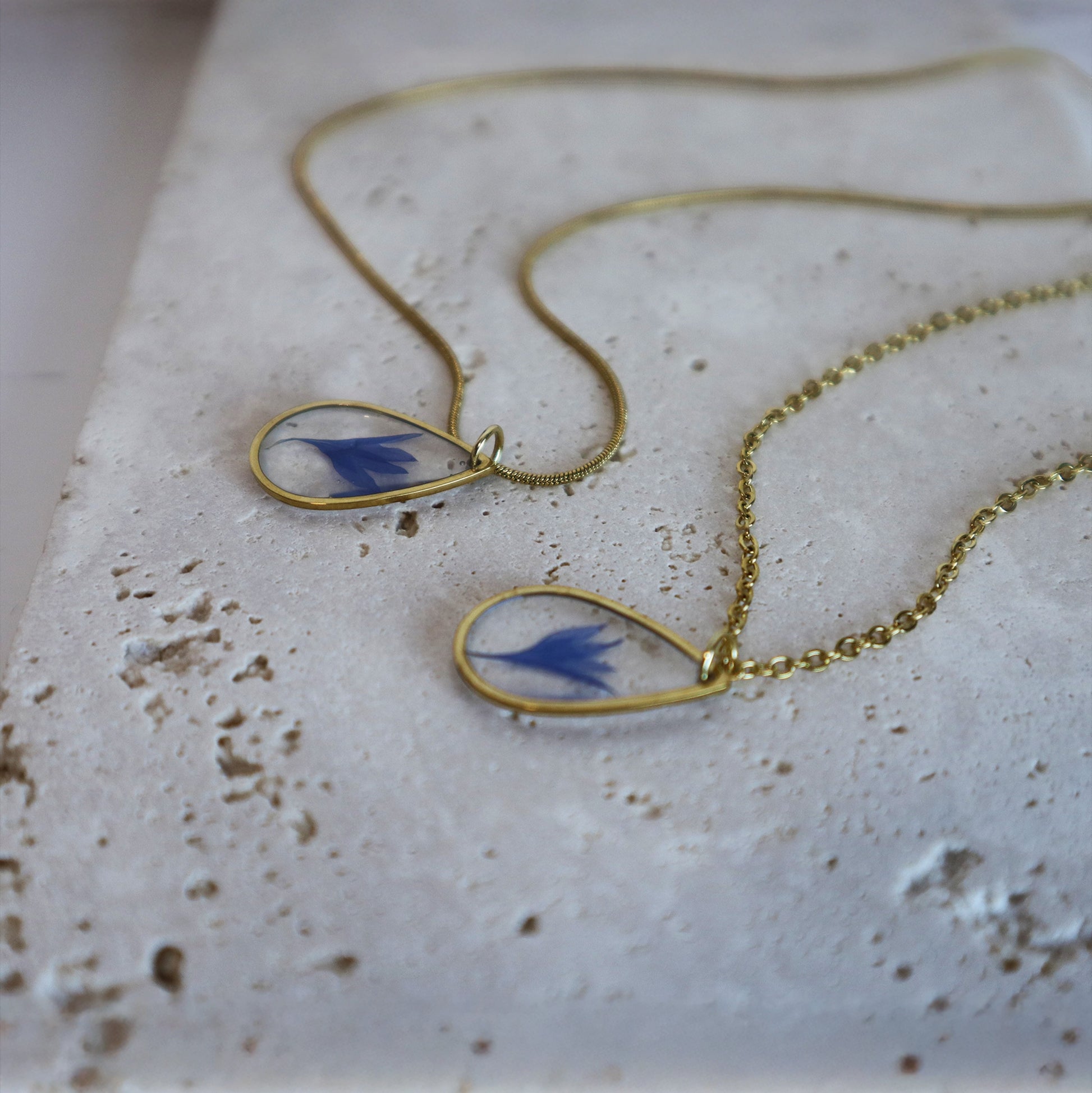 Drupt gouden ketting met druppelvormige hanger en echte blauwe korenbloem op een stenen ondergrond
