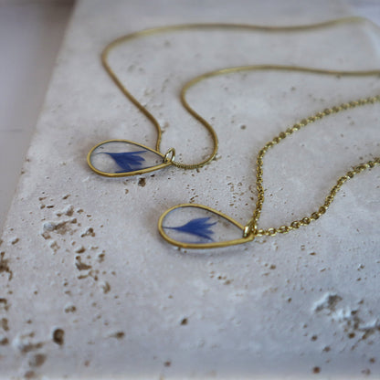 Drupt gouden ketting met druppelvormige hanger en echte blauwe korenbloem op een stenen ondergrond
