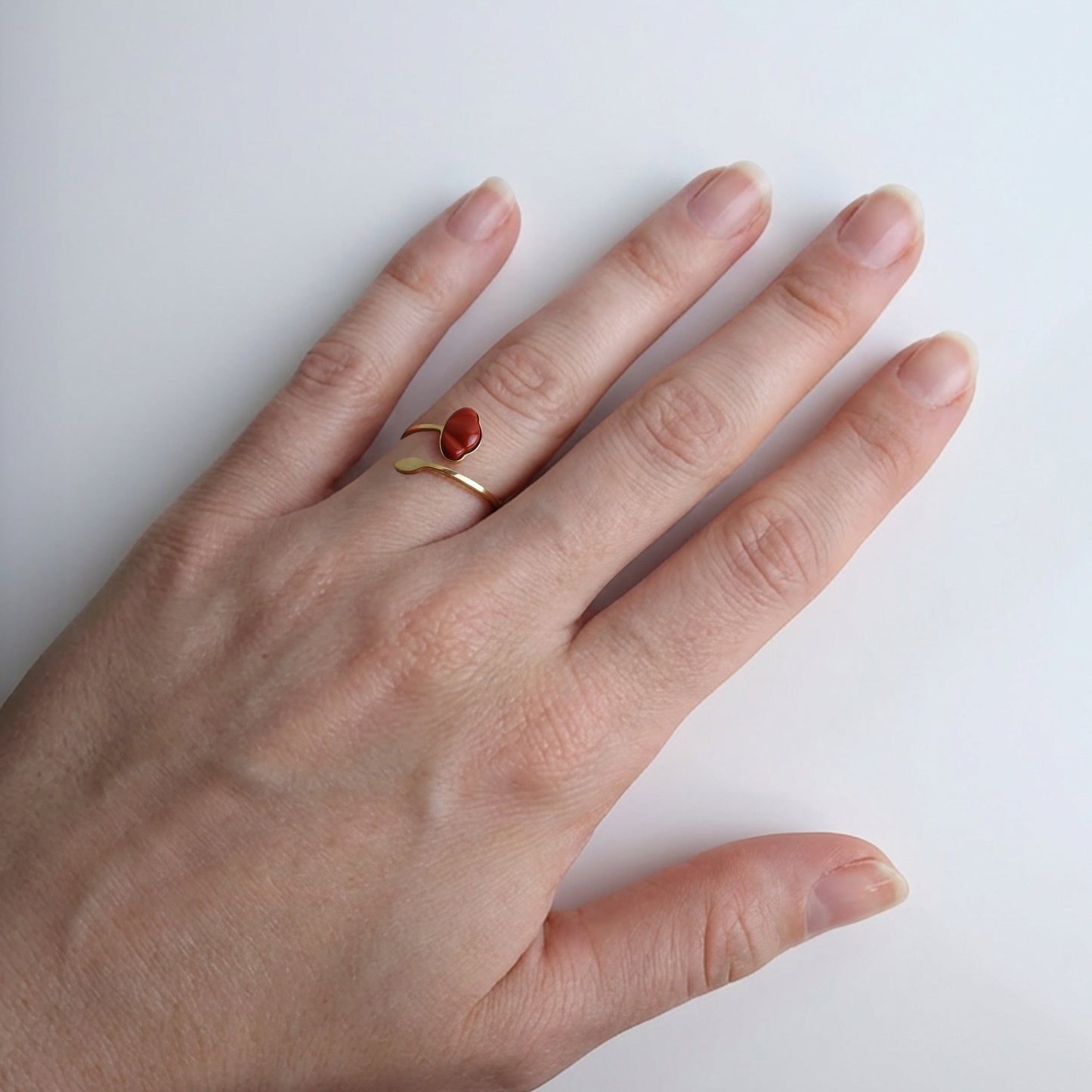 Drupt verstelbare ring van goud met een rode jaspis edelsteen in de vorm van een klaproos om een vinger