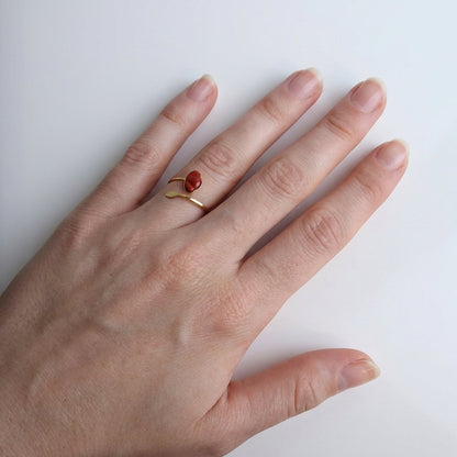 Drupt verstelbare ring van goud met een rode jaspis edelsteen in de vorm van een klaproos om een vinger