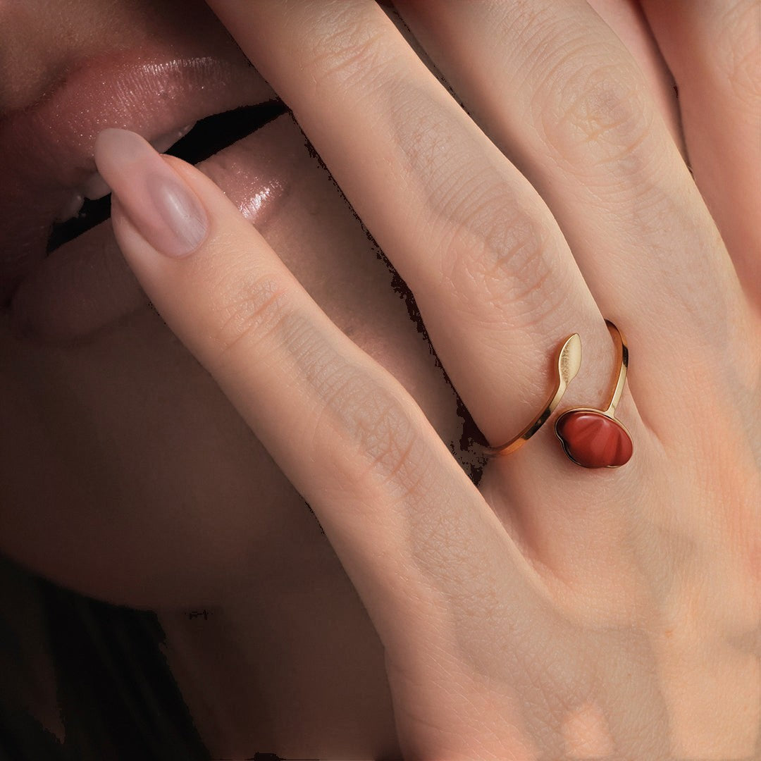 Drupt verstelbare gouden ring met een rode jaspis edelsteen in de vorm van een klaproos gedragen aan een vinger