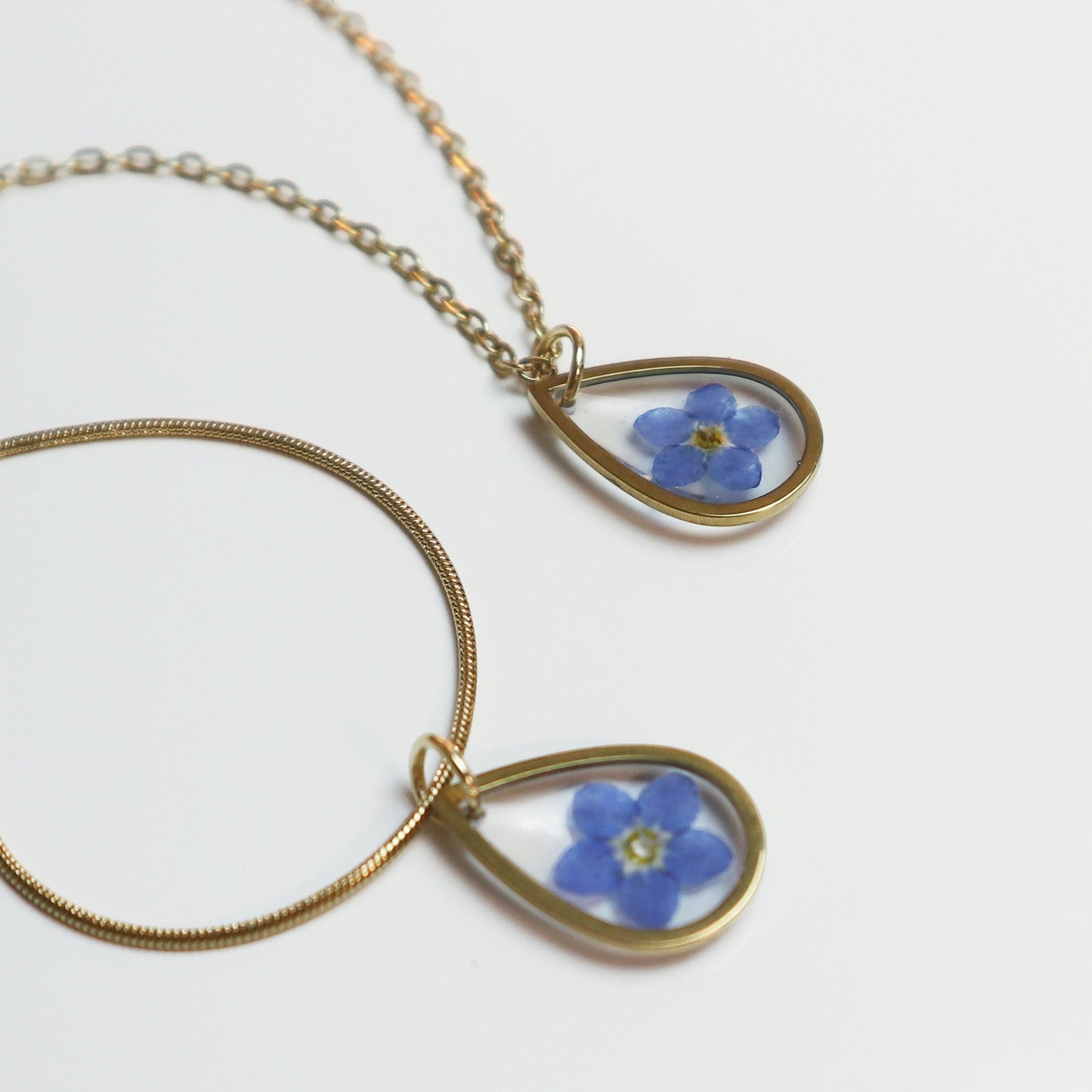 Drupt gouden ketting met druppelvormige hanger en een echt gedroogd blauw vergeet-mij-nietje bloemetje
