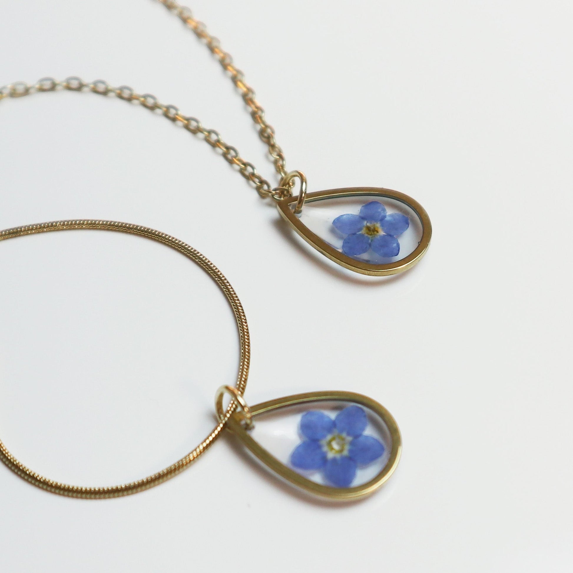 Drupt gouden ketting met druppelvormige hanger en een echt gedroogd blauw vergeet-mij-nietje bloemetje