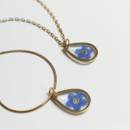 Drupt gouden ketting met druppelvormige hanger en een echt gedroogd blauw vergeet-mij-nietje bloemetje