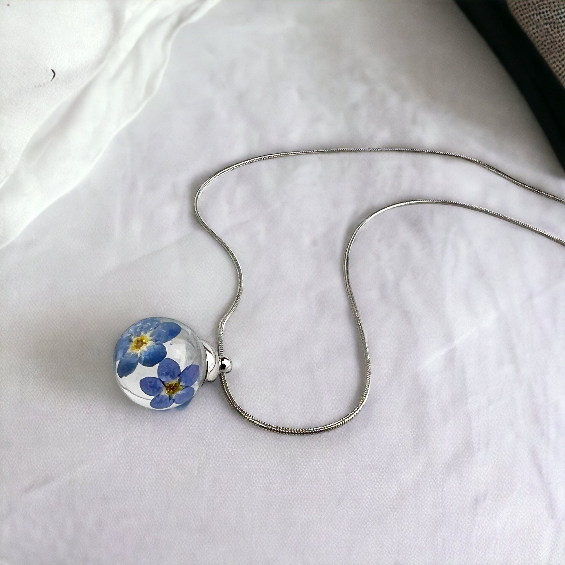 Drupt hanger Vergeet-me-niet met echte blauwe bloemen in een transparante bol aan een zilverkleurige ketting