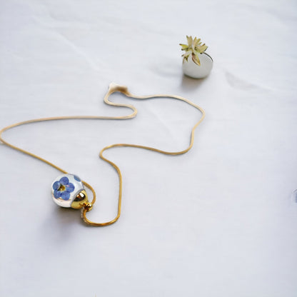 Drupt ketting met ronde hanger en echte blauwe vergeet-mij-nietjes in hars aan een goudkleurige slangenketting
