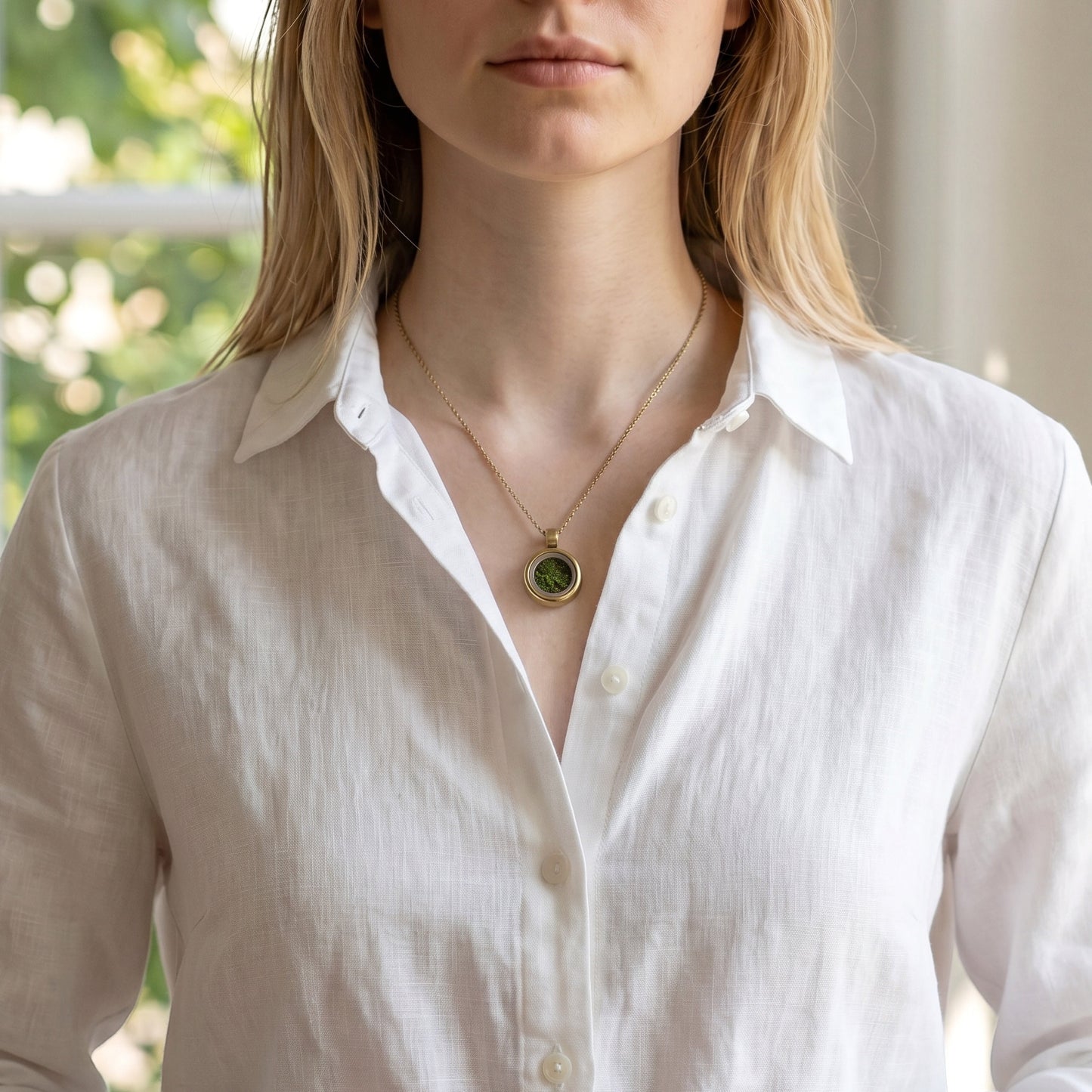 Drupt Koester hanger in goud gedragen aan een ketting met een dierbare herinnering erin op een wit linnen overhemd.