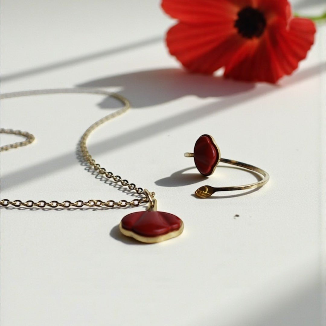 Drupt ring en hanger met rode jaspis edelsteen in de vorm van een klaproos, gezet in goud op een witte ondergrond.