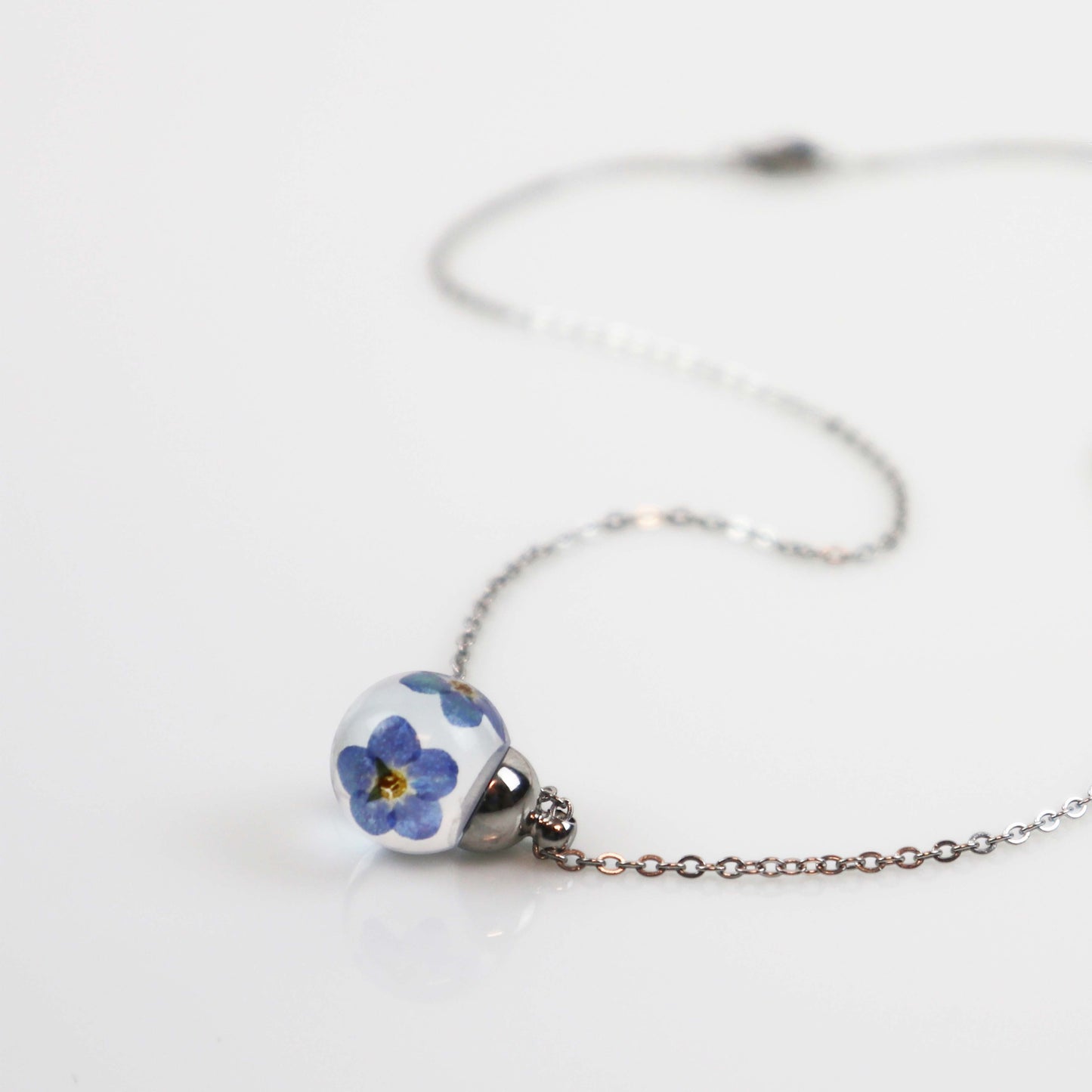 Drupt hanger Vergeet-me-niet met echte blauwe bloemen in een transparante bol aan een zilverkleurige ketting.