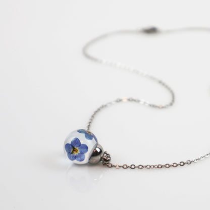 Drupt hanger Vergeet-me-niet met echte blauwe bloemen in een transparante bol aan een zilverkleurige ketting.