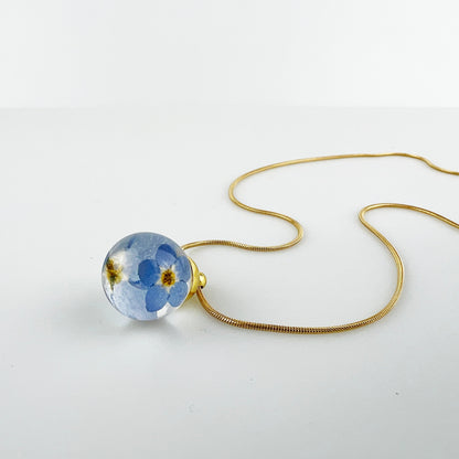 Drupt hanger met twee gedroogde blauwe vergeet-mij-nietjes in een transparante bol aan een gouden ketting