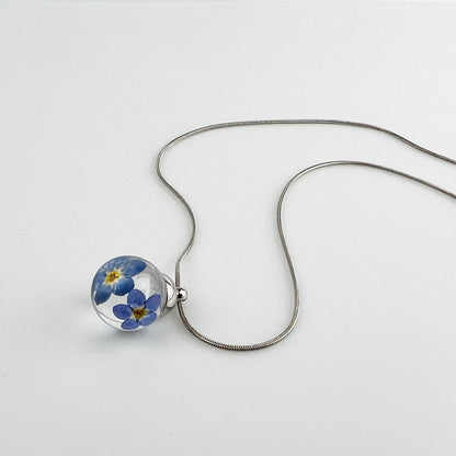 Drupt hanger met twee blauwe vergeet-mij-nietjes in een transparante bol aan een zilverkleurige ketting.