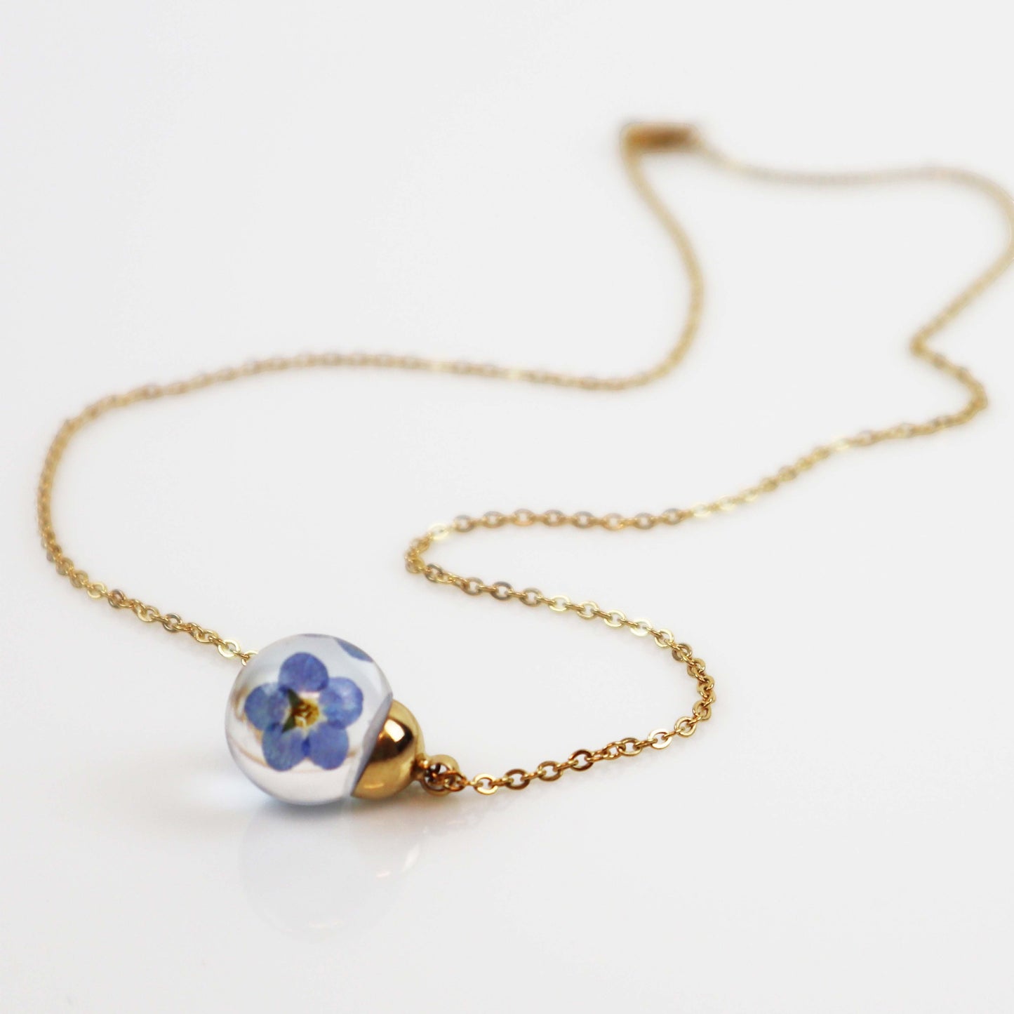 Drupt ketting met ronde glazen hanger waarin echte blauwe vergeet-mij-nietjes zijn verwerkt aan een fijne gouden ketting