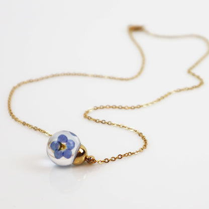 Drupt ketting met ronde glazen hanger waarin echte blauwe vergeet-mij-nietjes zijn verwerkt aan een fijne gouden ketting
