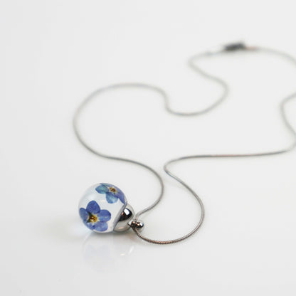 Drupt ketting met ronde hanger en echte blauwe vergeet-mij-nietjes in krasvaste hars op een zilverkleurige ketting.