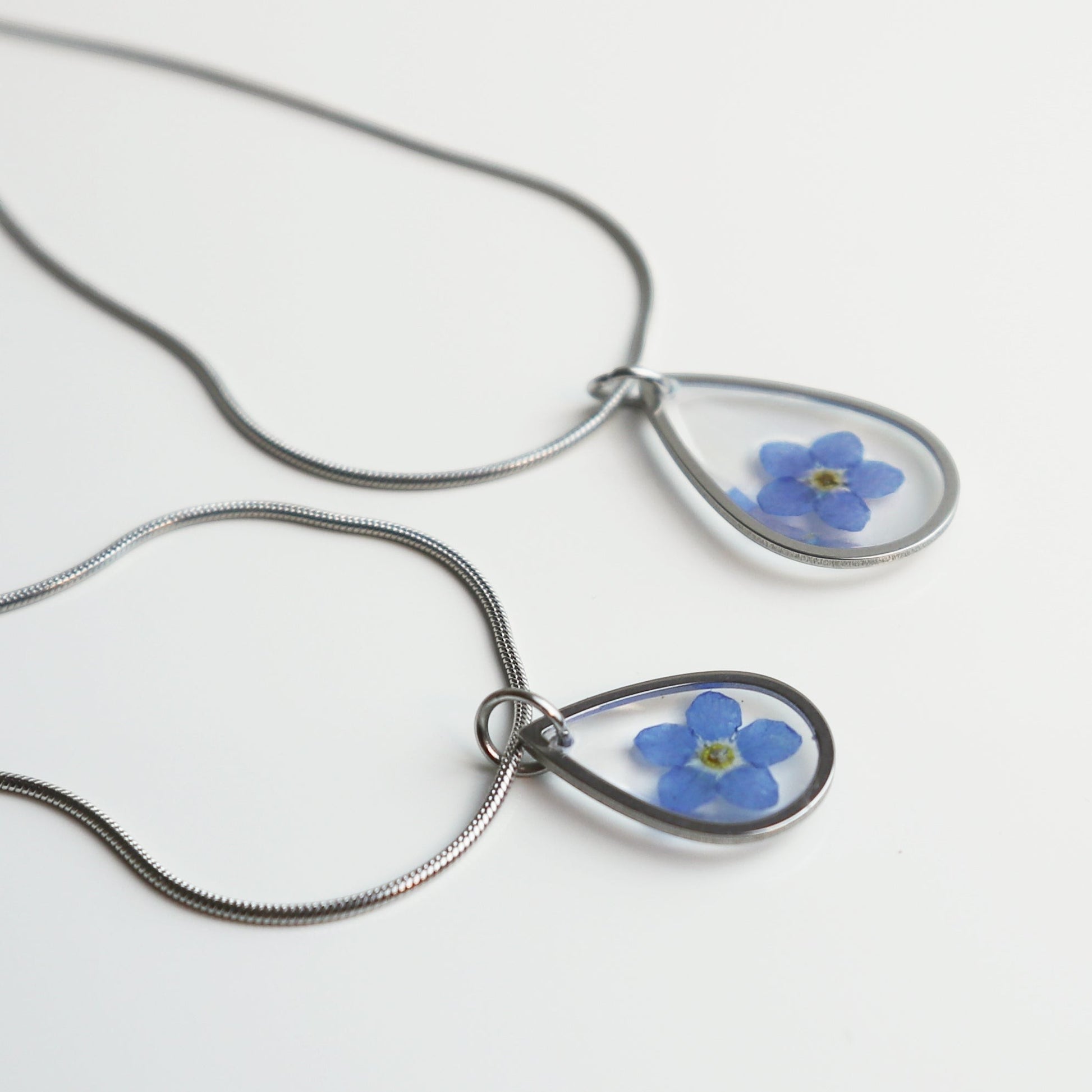 Drupt zilveren druppelvormige ketting met een echt gedroogd blauw vergeet-mij-nietje in een minimalistisch design.