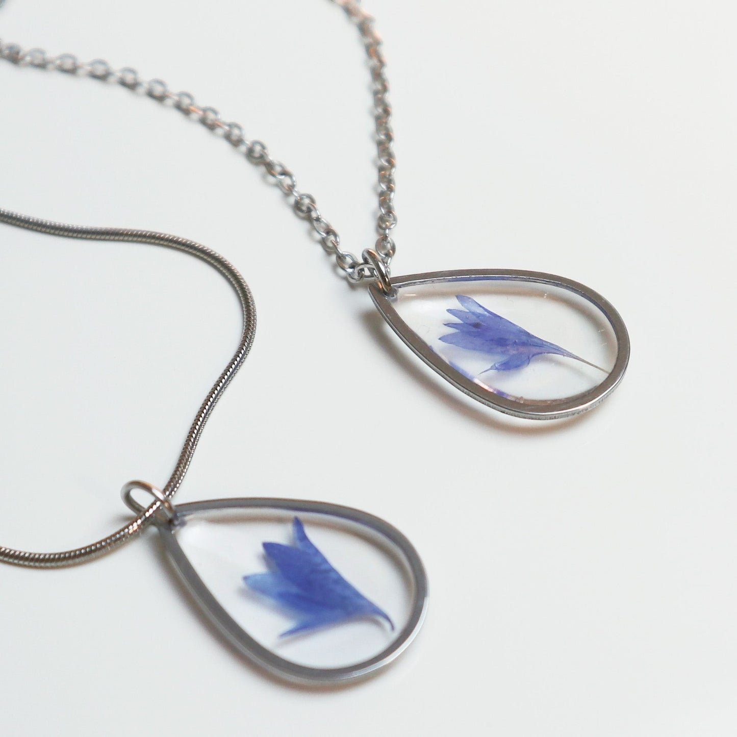 Drupt zilveren druppelvormige hanger met een echte blauwe korenbloem in hars, minimalistisch handgemaakt sieraad.