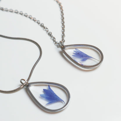 Drupt zilveren druppelvormige hanger met een echte blauwe korenbloem in hars, minimalistisch handgemaakt sieraad.
