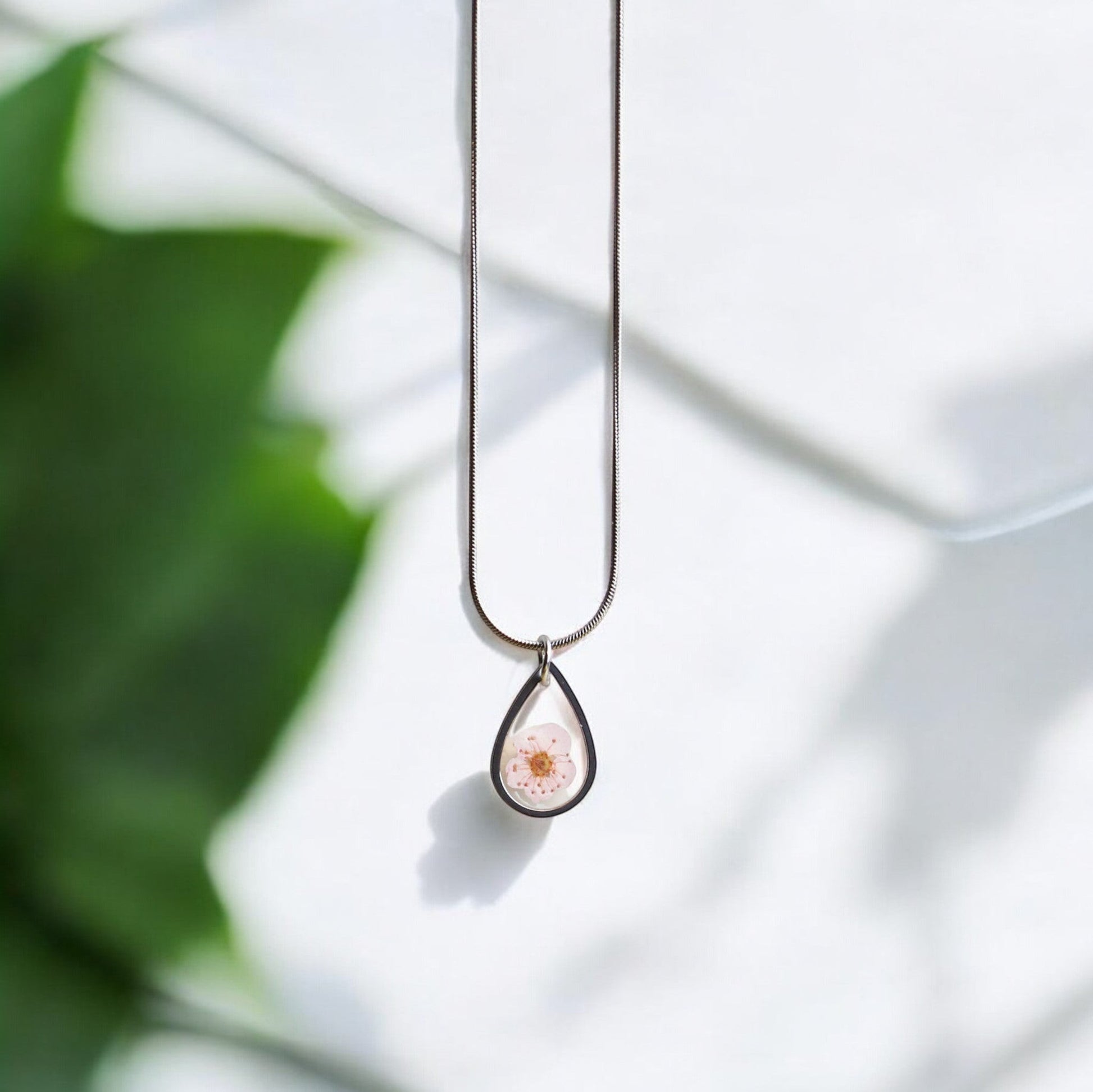 Drupt ketting met zilveren druppelvormige hanger en een delicate roze pruimenbloesem in hars.