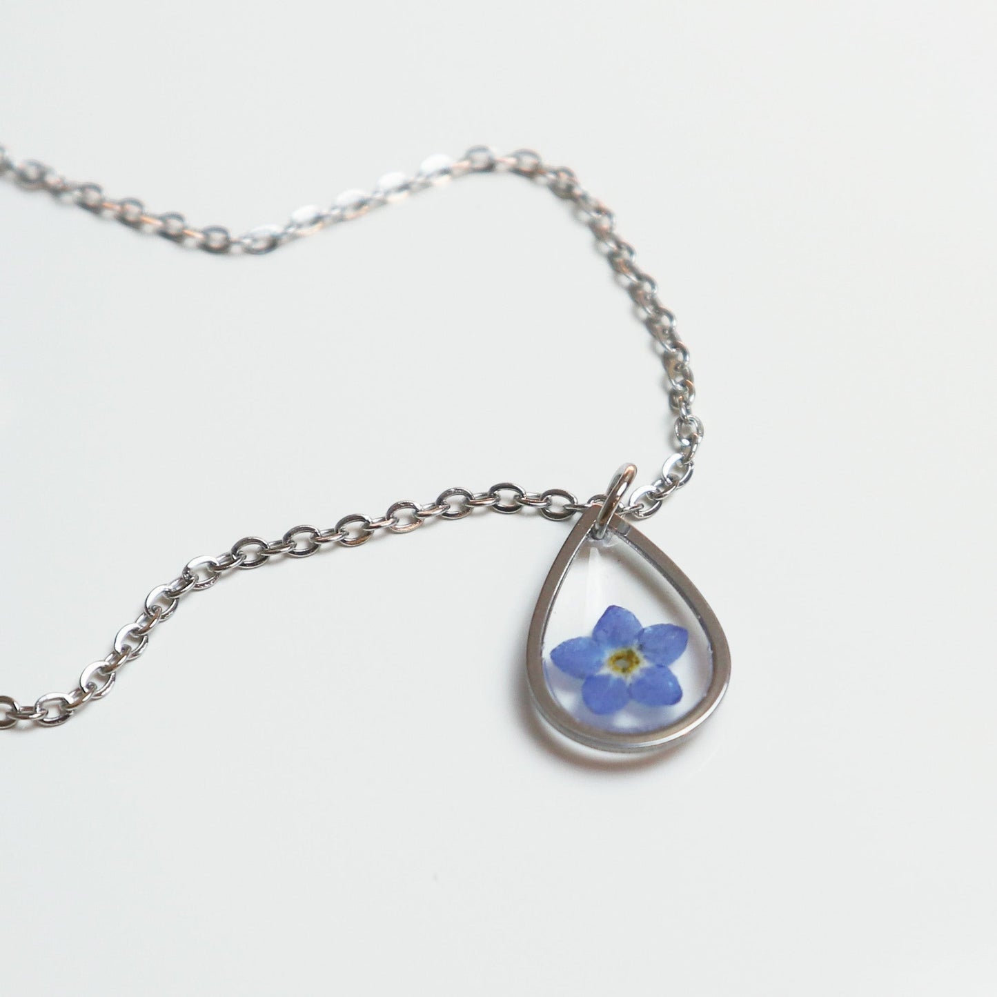 Drupt zilveren druppelvormige hanger met een echt gedroogd blauw vergeet-mij-nietje aan een fijne ketting.