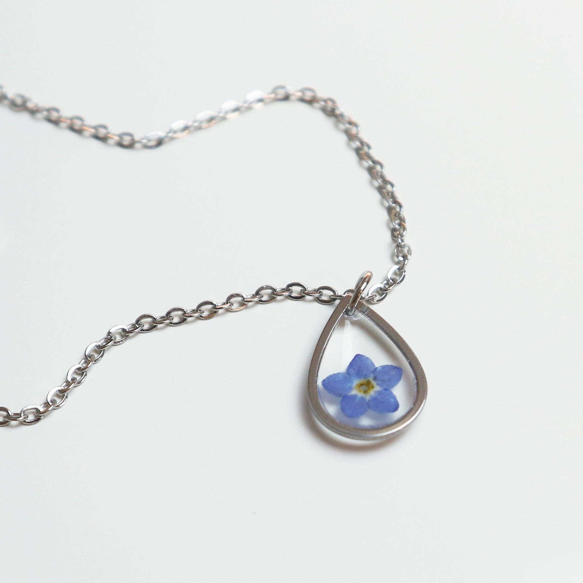Drupt zilveren druppelvormige hanger met een echt gedroogd blauw vergeet-mij-nietje aan een fijne ketting.