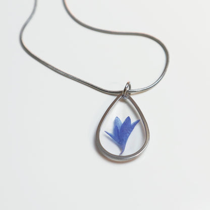 Drupt zilveren druppelvormige hanger met een echte blauwe korenbloem, minimalistisch handgemaakt sieraad aan ketting.